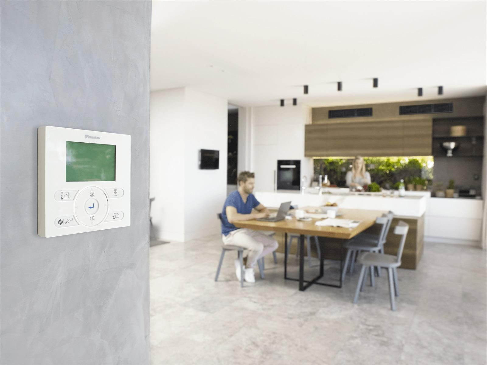 A Man Is Sitting At A Table In A Kitchen Using A Laptop Computer — Jervis Bay Airconditioning In Albion Park, NSW