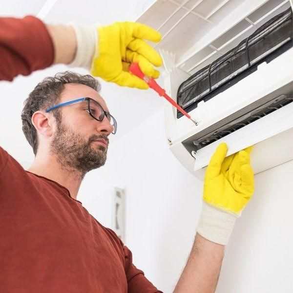 A Man Wearing Yellow Gloves Is Fixing An Air Conditioner With A Screwdriver — Jervis Bay Airconditioning In Berry, NSW