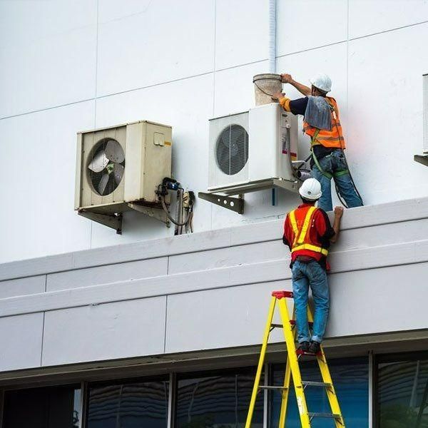 Two Men Are Working On An Air Conditioner On The Side Of A Building — Jervis Bay Airconditioning In Nowra, NSW