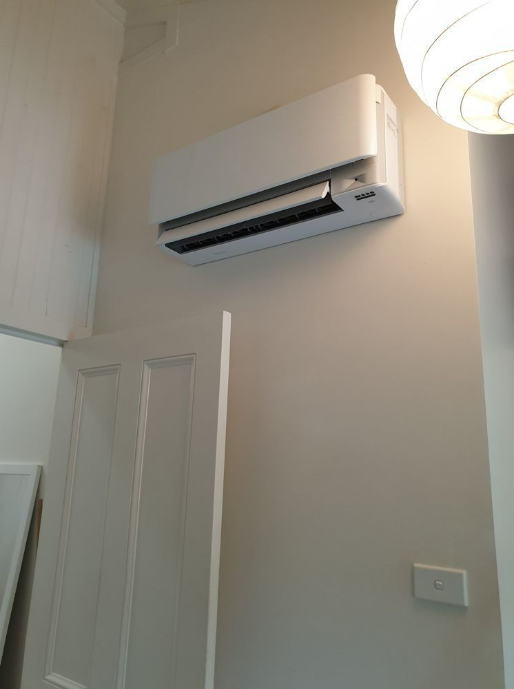 A White Air Conditioner Is Hanging On A Wall Next To A Door — Jervis Bay Airconditioning In Huskisson, NSW