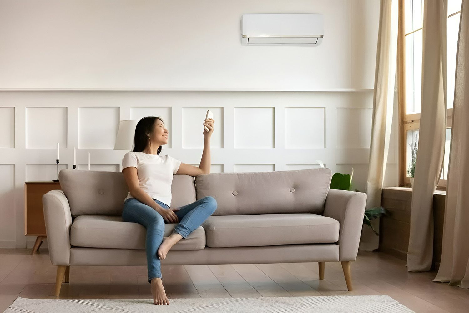 Woman Sits on a Sofa, Using a Remote to Control an Air Conditioner