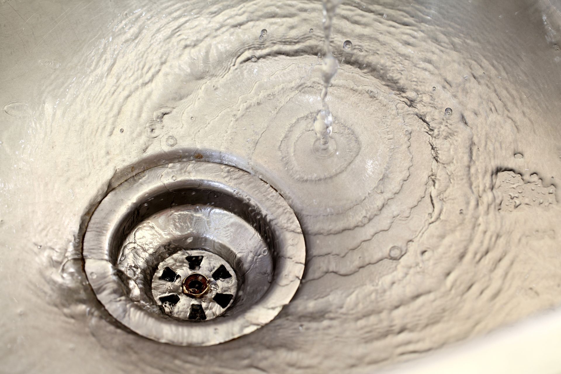 Water swirling down a stainless steel sink drain.