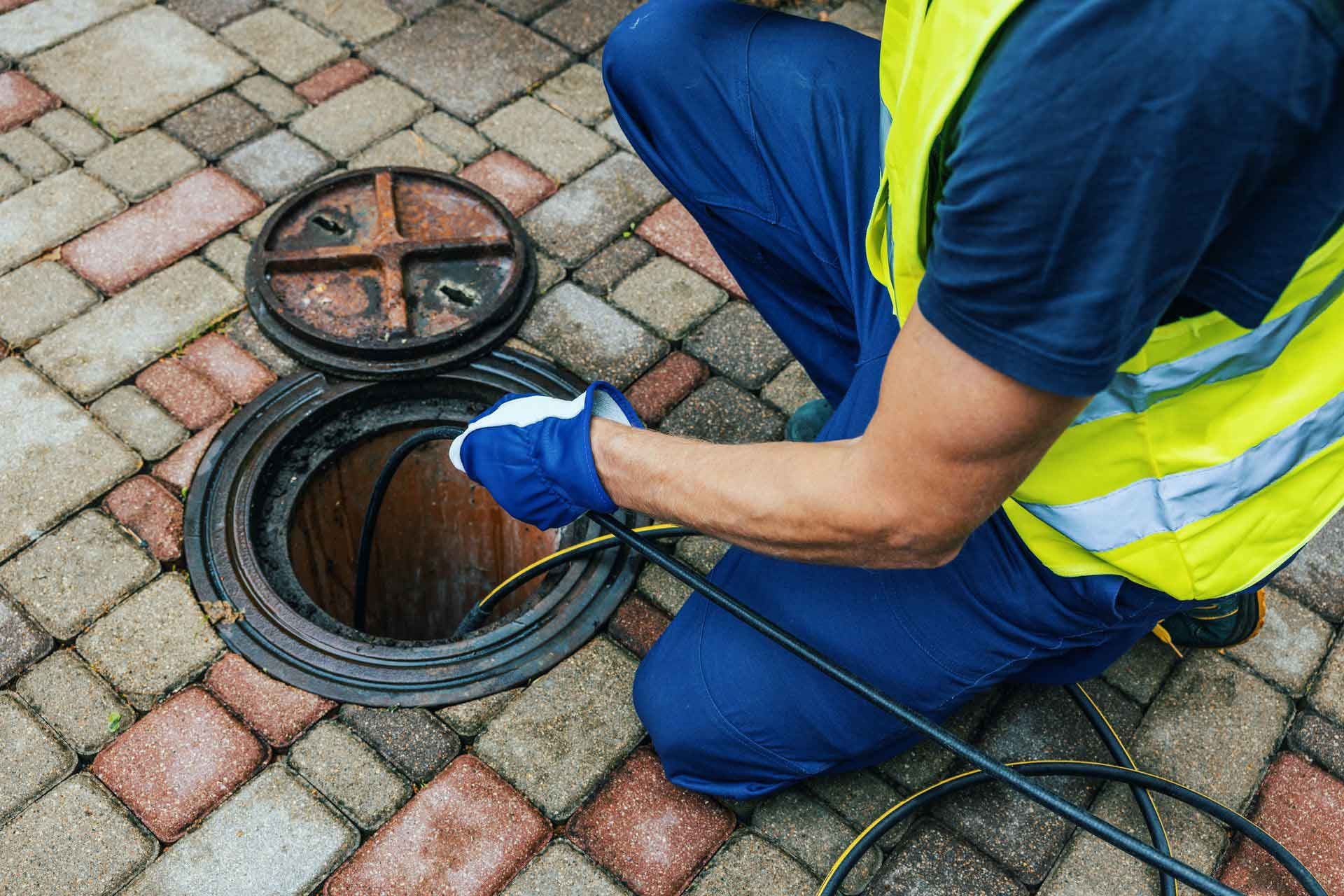 A man wearing a safety vest is repairing a drain, contributing to sewer line system cleaning.