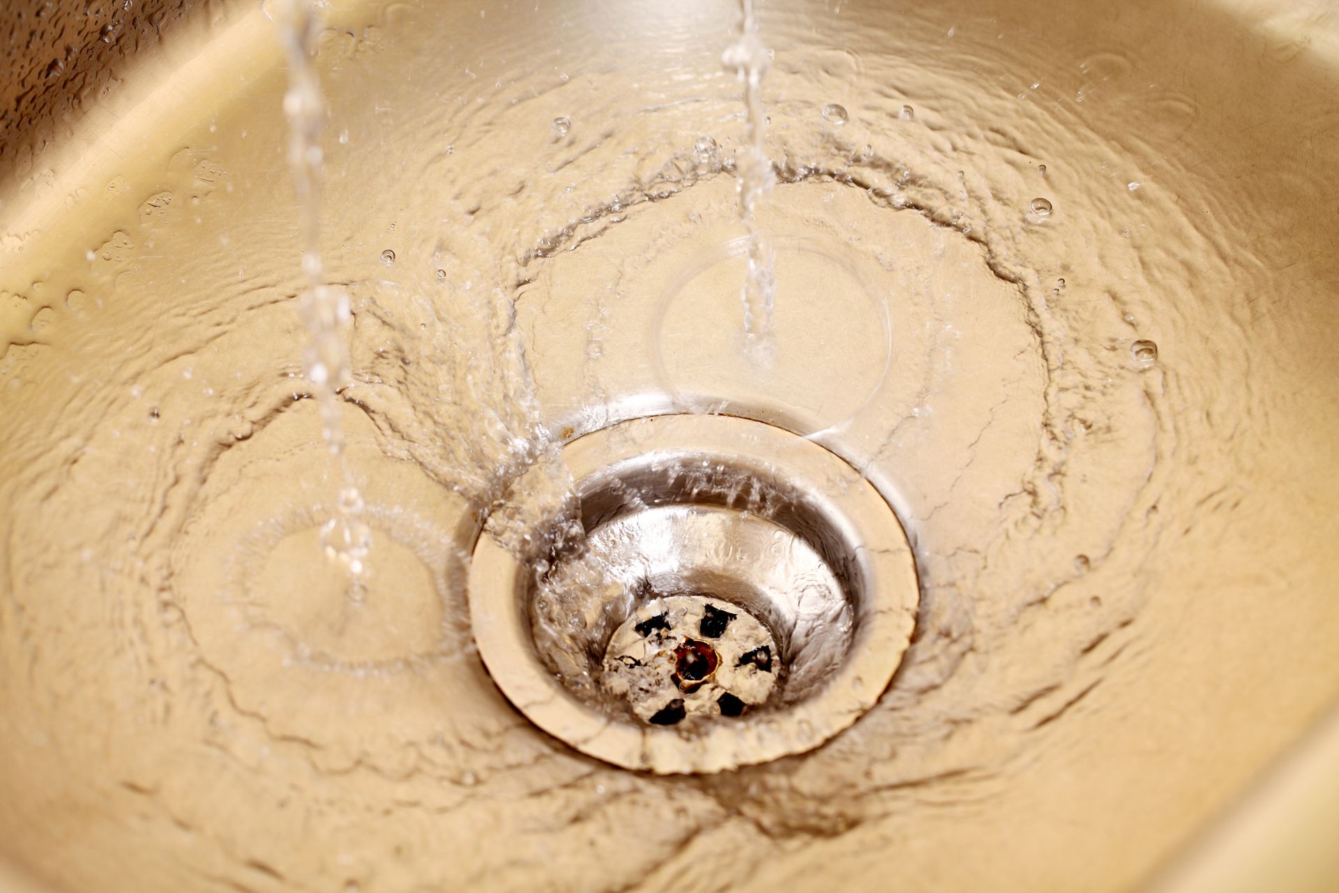 Water flowing into a stainless steel sink drain.