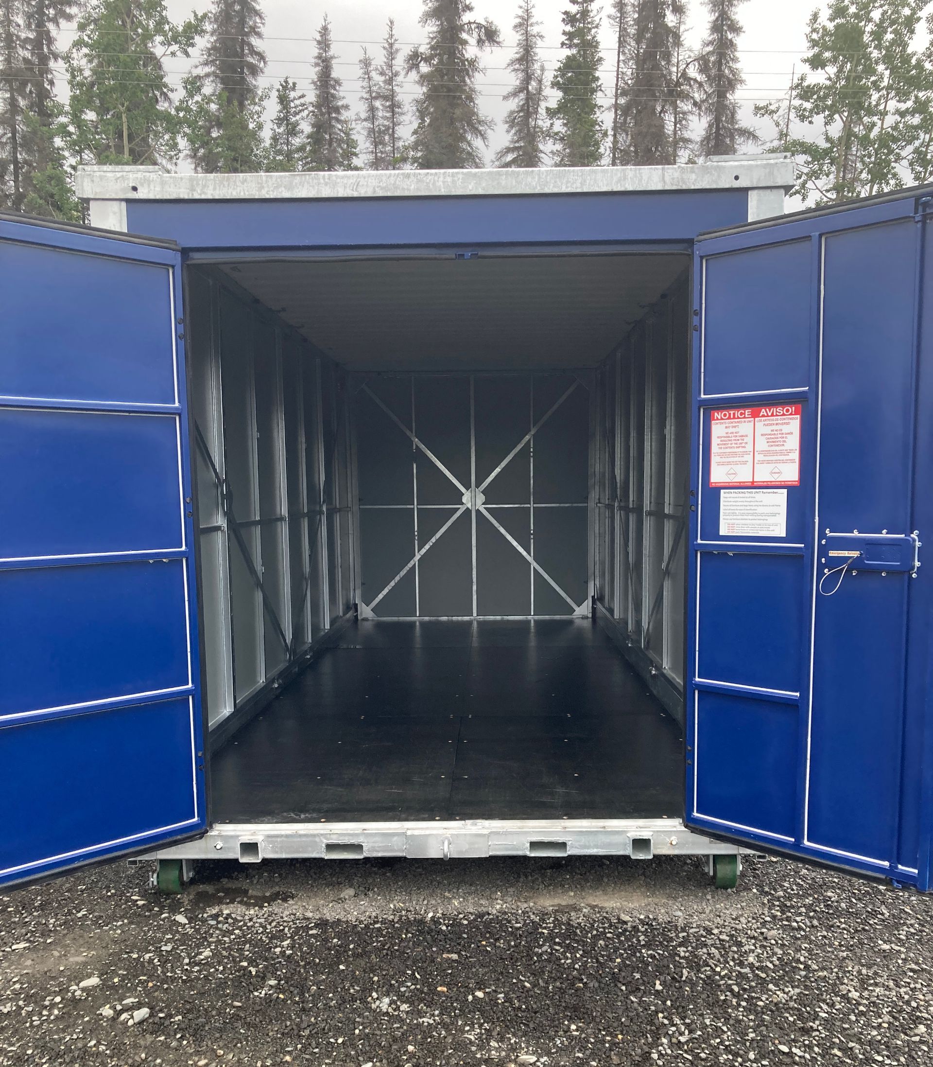 A blue shipping container with the doors open and a warning sign on the door.