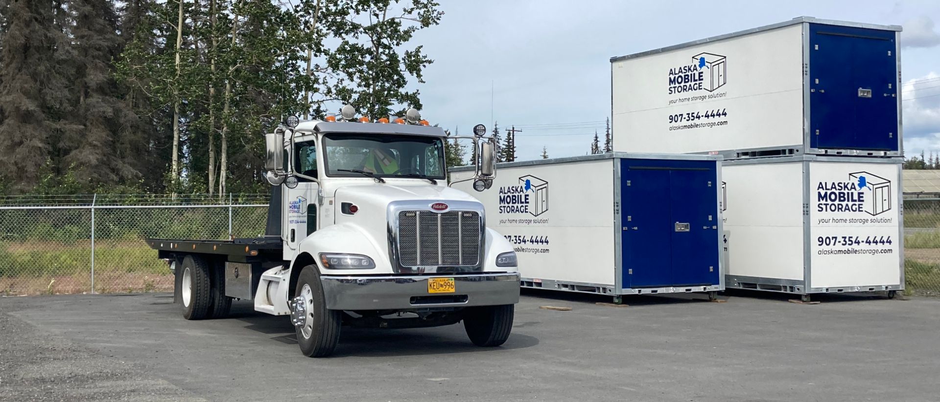 A white semi truck is parked next to a row of blue and white containers.