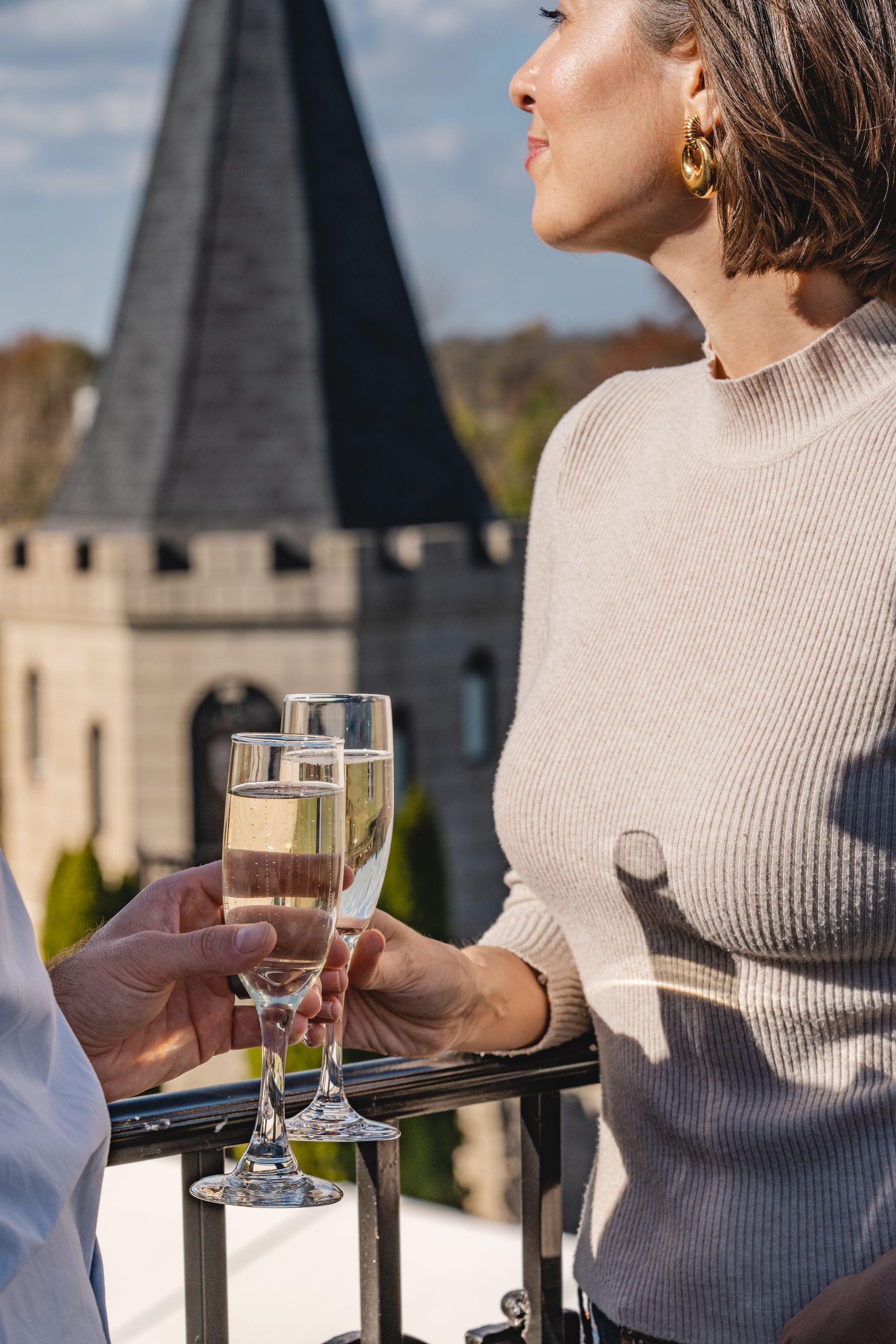 Woman toasting champagne on a balcony, with a castle tower in the background.