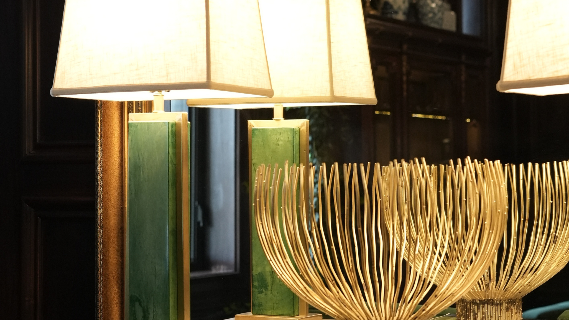 Green lamp with white shade next to a golden wire bowl.