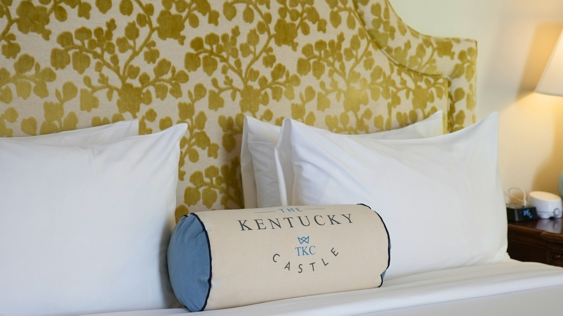 A bed with a floral headboard and "Kentucky Castle" pillow.