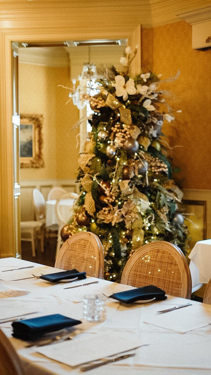 A decorated Christmas tree sits next to a table set for a meeting or event in a warm-toned room.