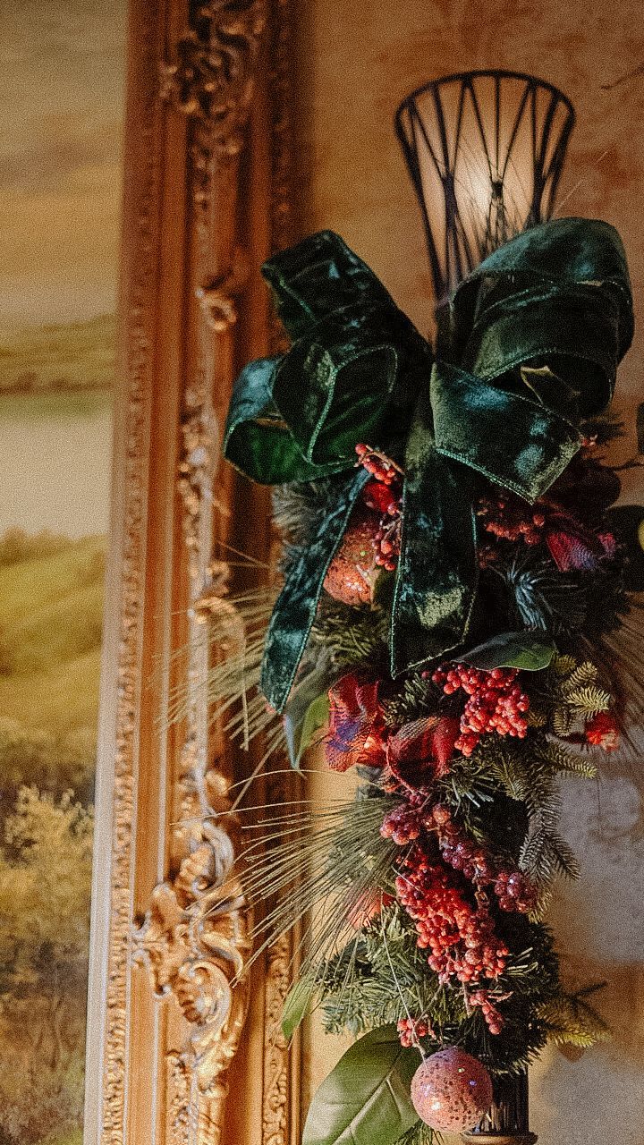 Christmas garland with large green bow and red berries on ornate frame.