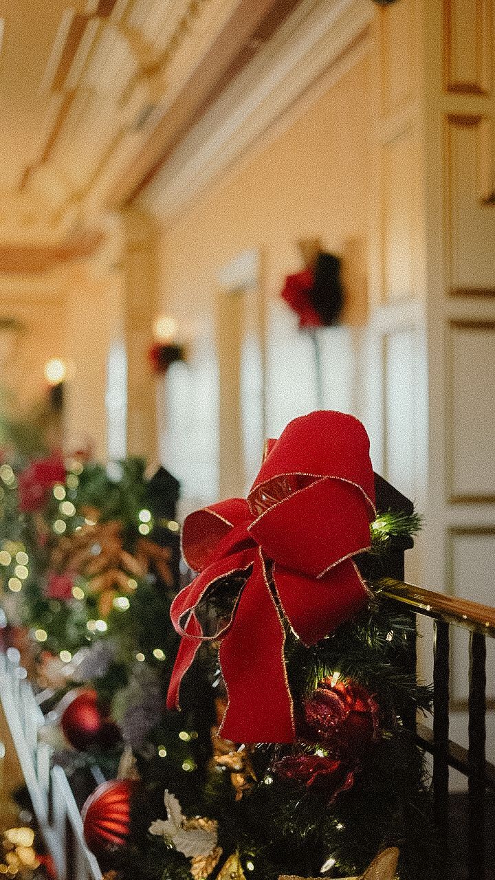 A festive Christmas scene with a red bow on decorated greenery along a hallway.