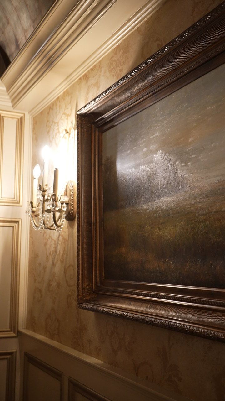 Ornate framed painting on a wall with a sconce, featuring a landscape.