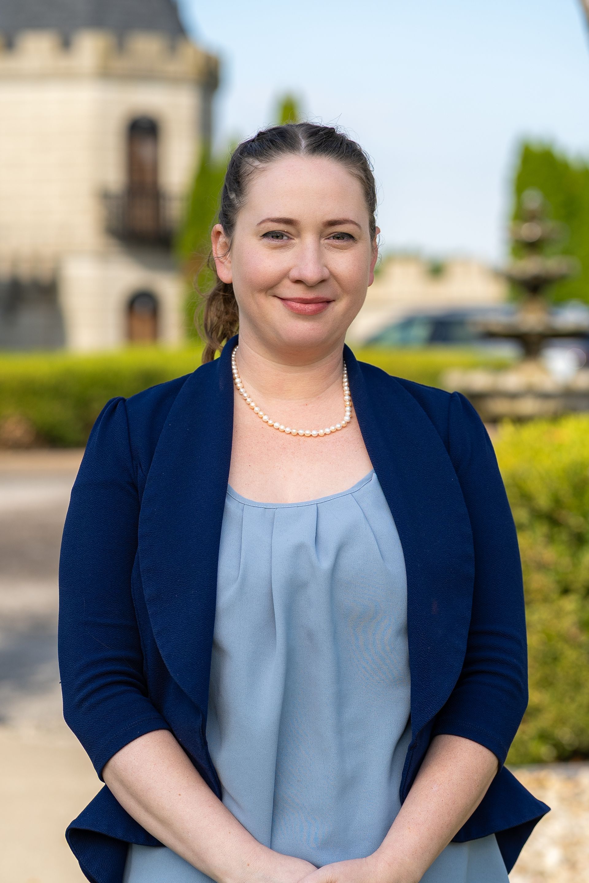 Chef in black uniform, glasses, smiling in a kitchen, ovens in background.