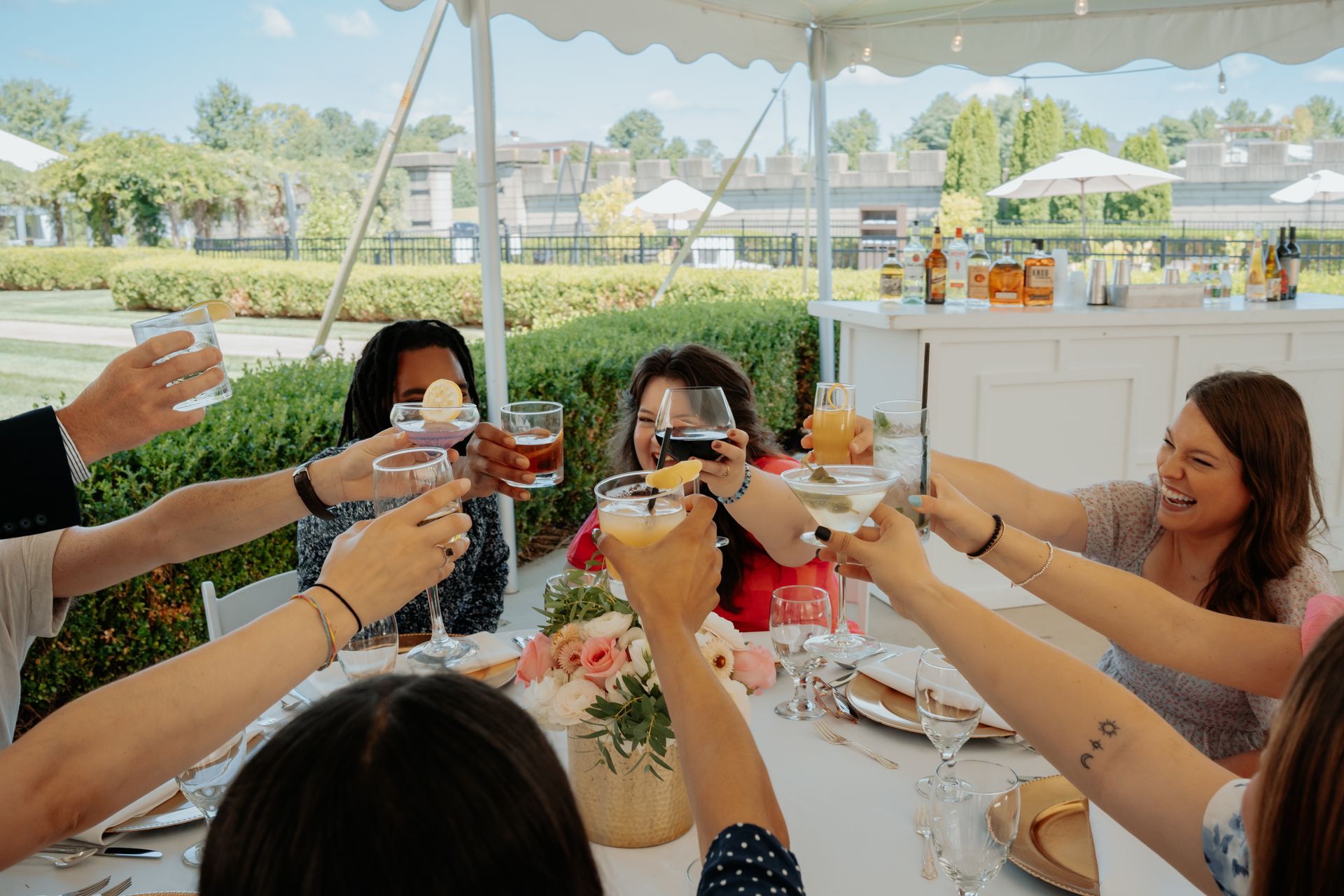 People toasting drinks at an outdoor celebration under a white tent.