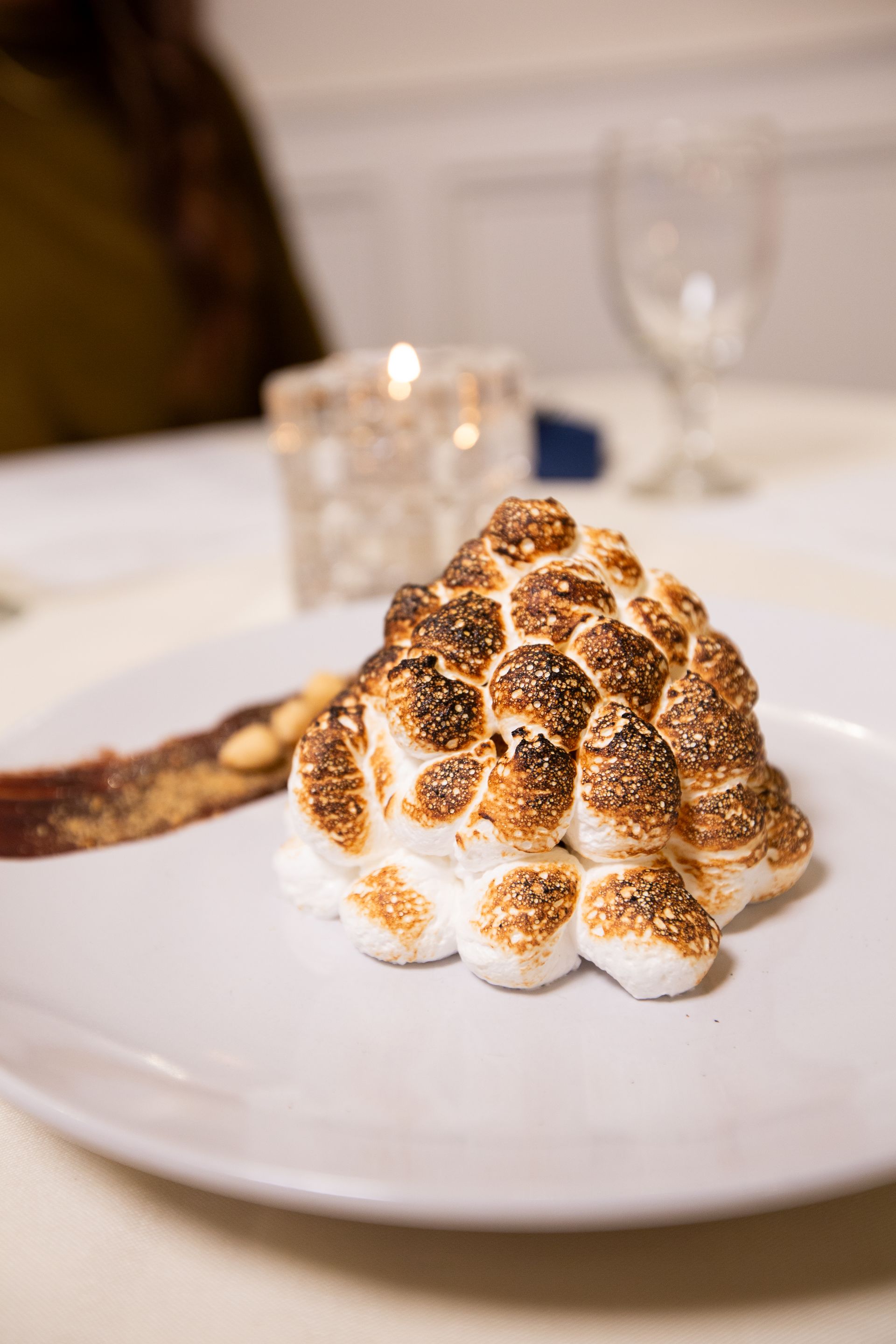 Toasted meringue dessert on a white plate, with a biscuit and a candle in the background.