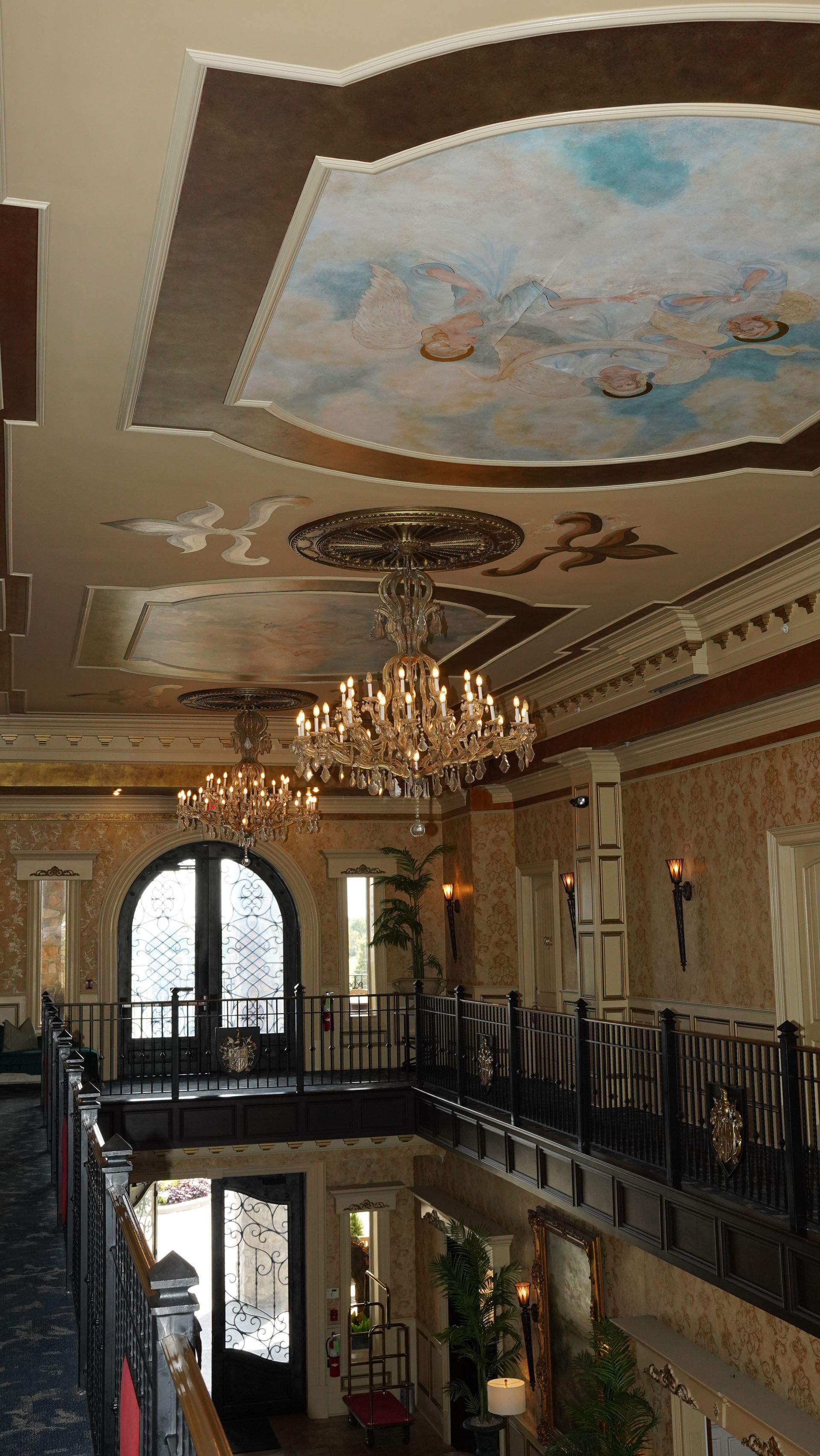 A grand hallway with chandeliers, balcony, and detailed ceiling art.