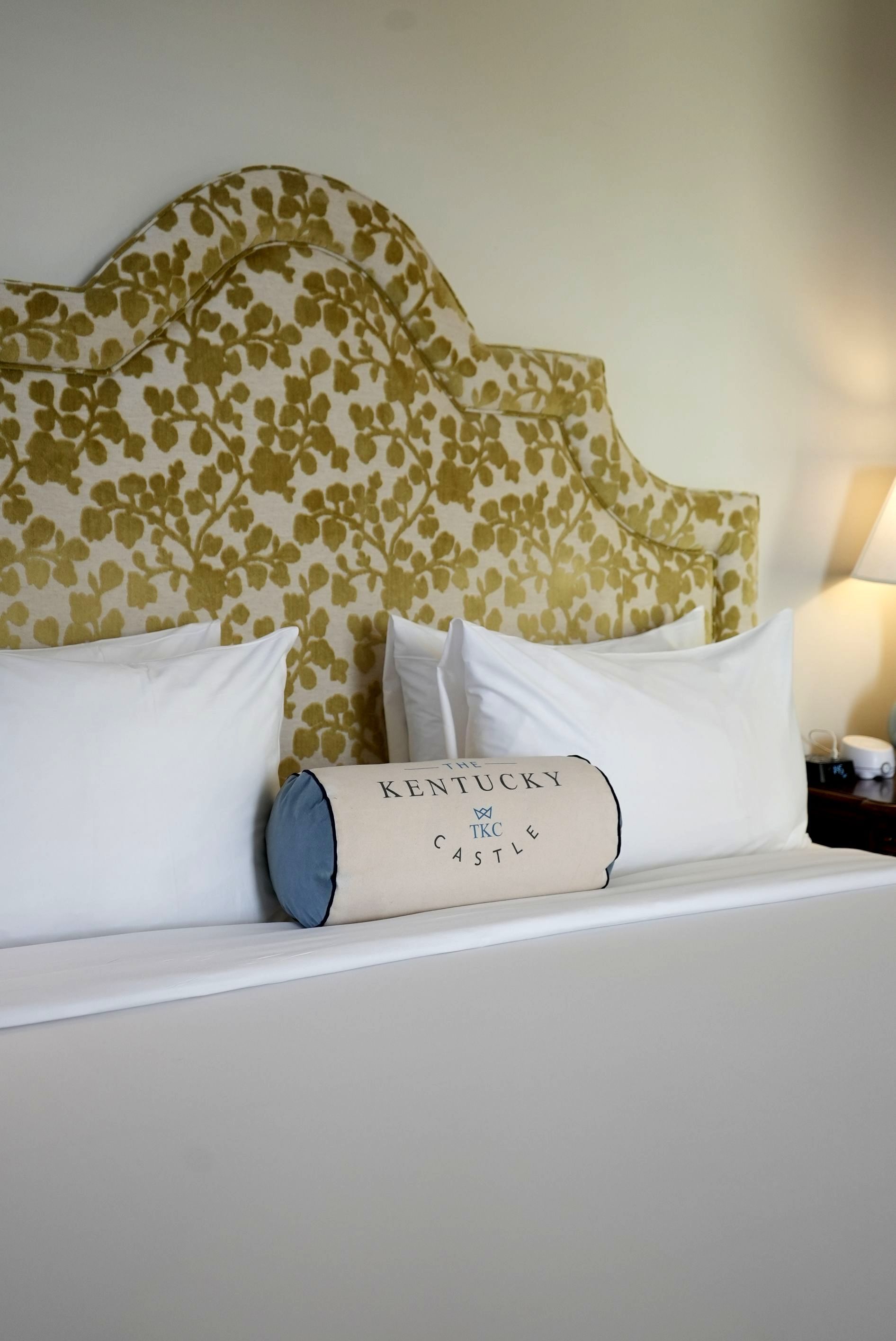 Bed with a floral headboard, white pillows, and a bolster pillow with text.