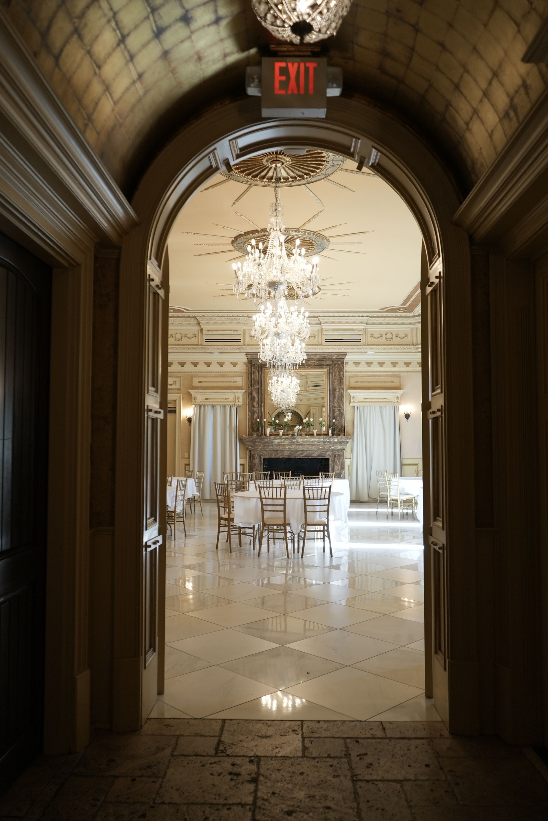 Archway leads to a formal dining room with chandeliers, a fireplace, and a table set for a meal.