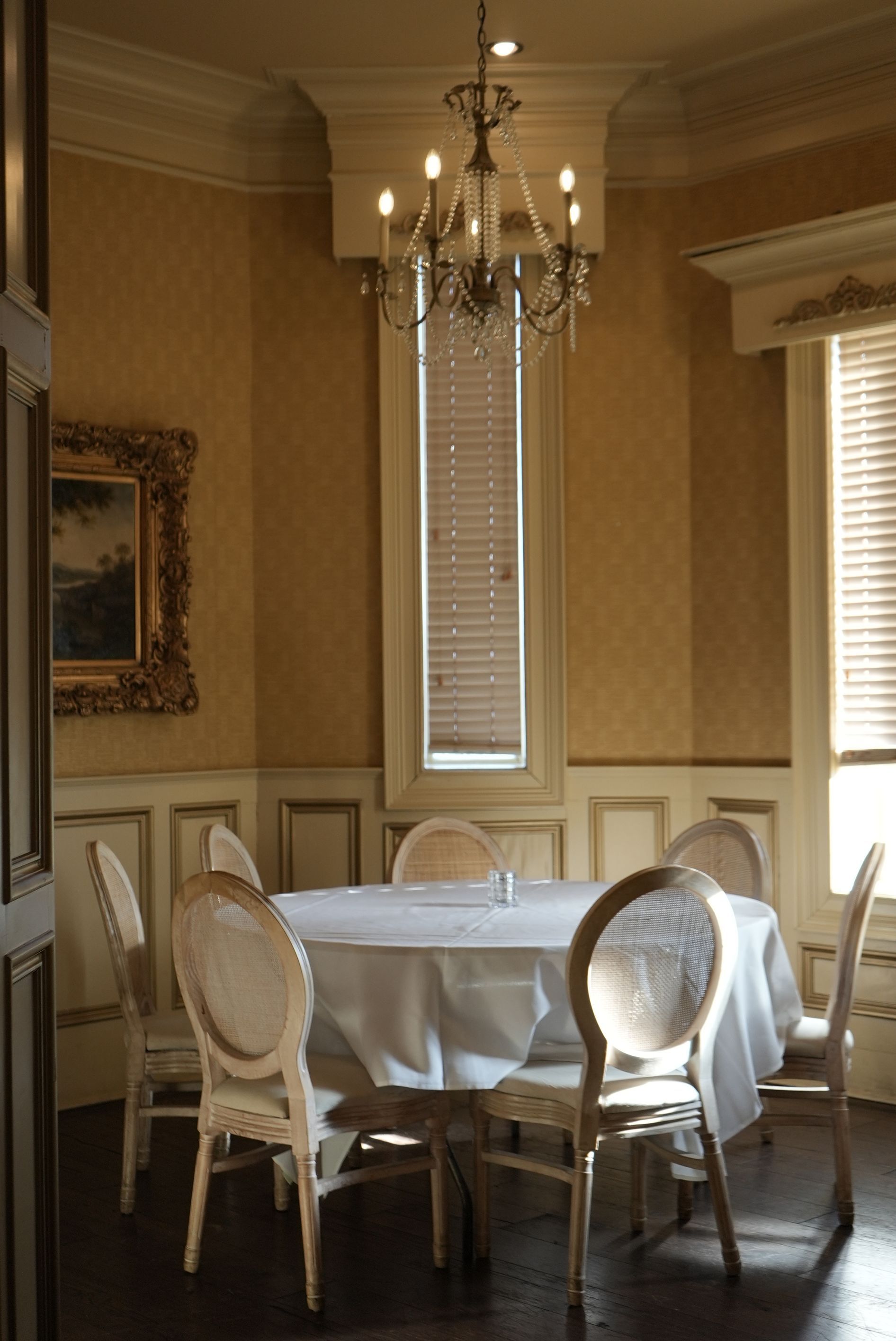 Round dining table set for six, in a room with gold wallpaper, chandelier and ornate trim.