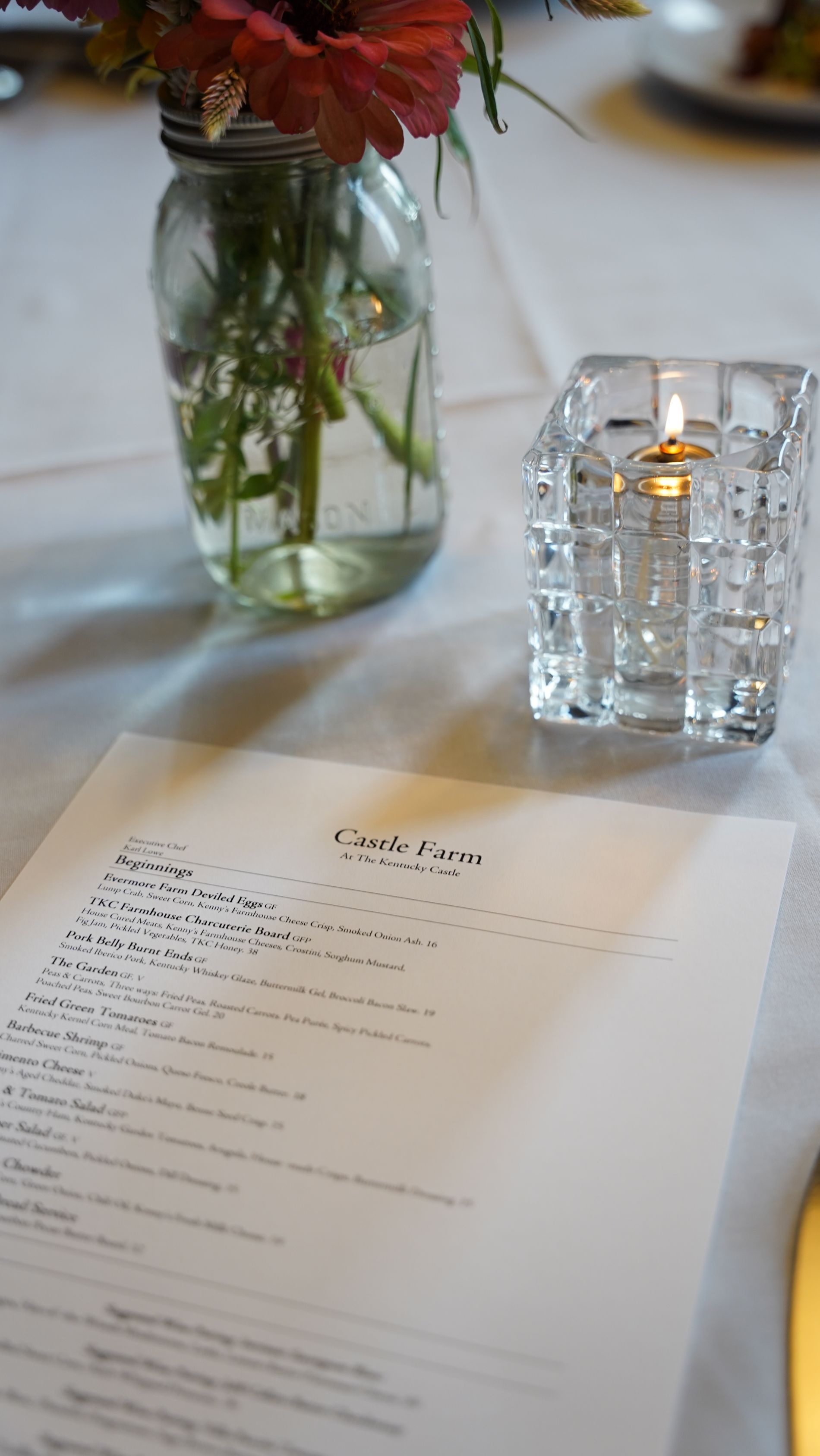 Menu on a white tablecloth with a vase of flowers and a candle.
