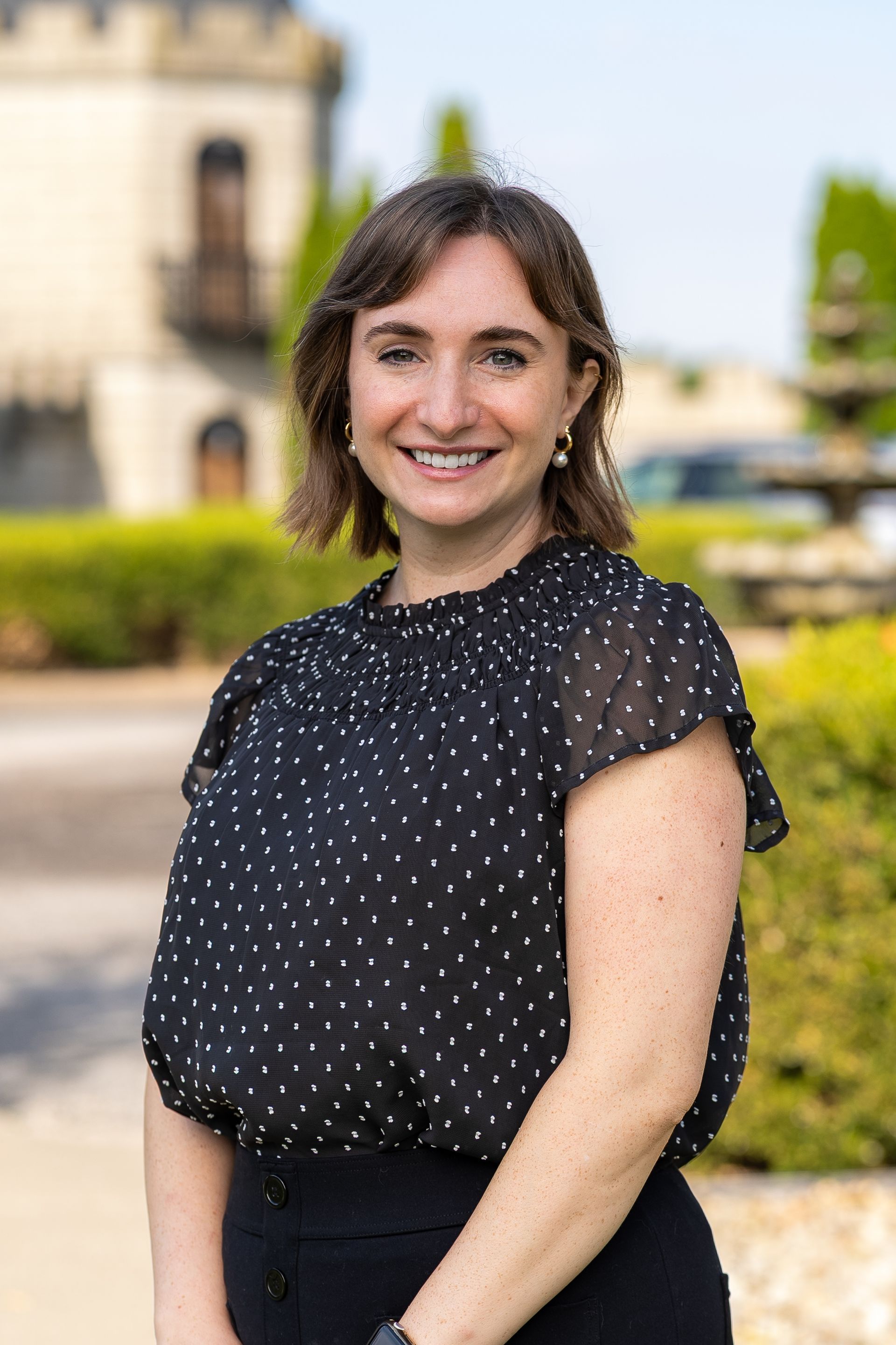 Woman with long brown curly hair in blue polka dot dress smiles, leaning on a marble counter.