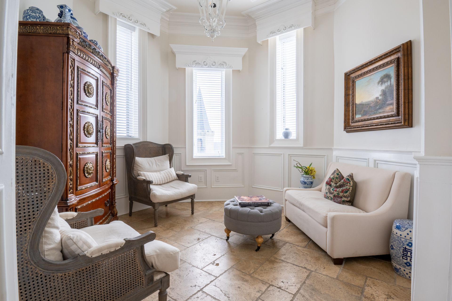 Elegant, bright sitting room with antique furniture, windows, beige sofa, and stone tile floor.