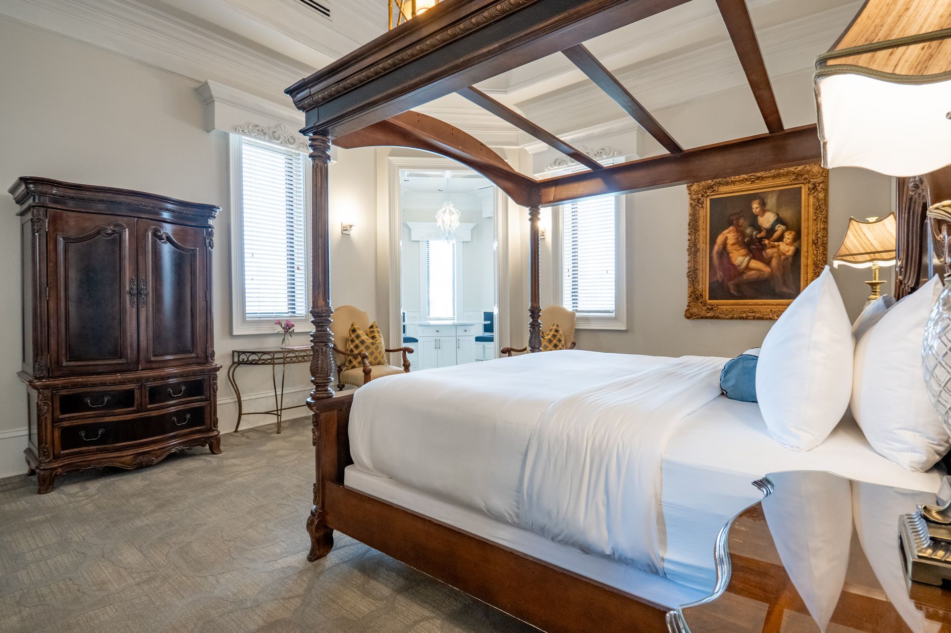 A grand bedroom with a canopy bed, antique wardrobe, and artwork.