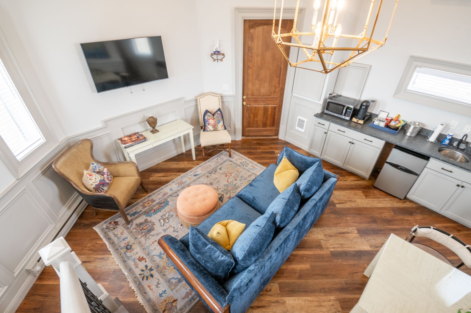 Cozy living area with blue sofa, small kitchen, wood floors, and neutral walls.