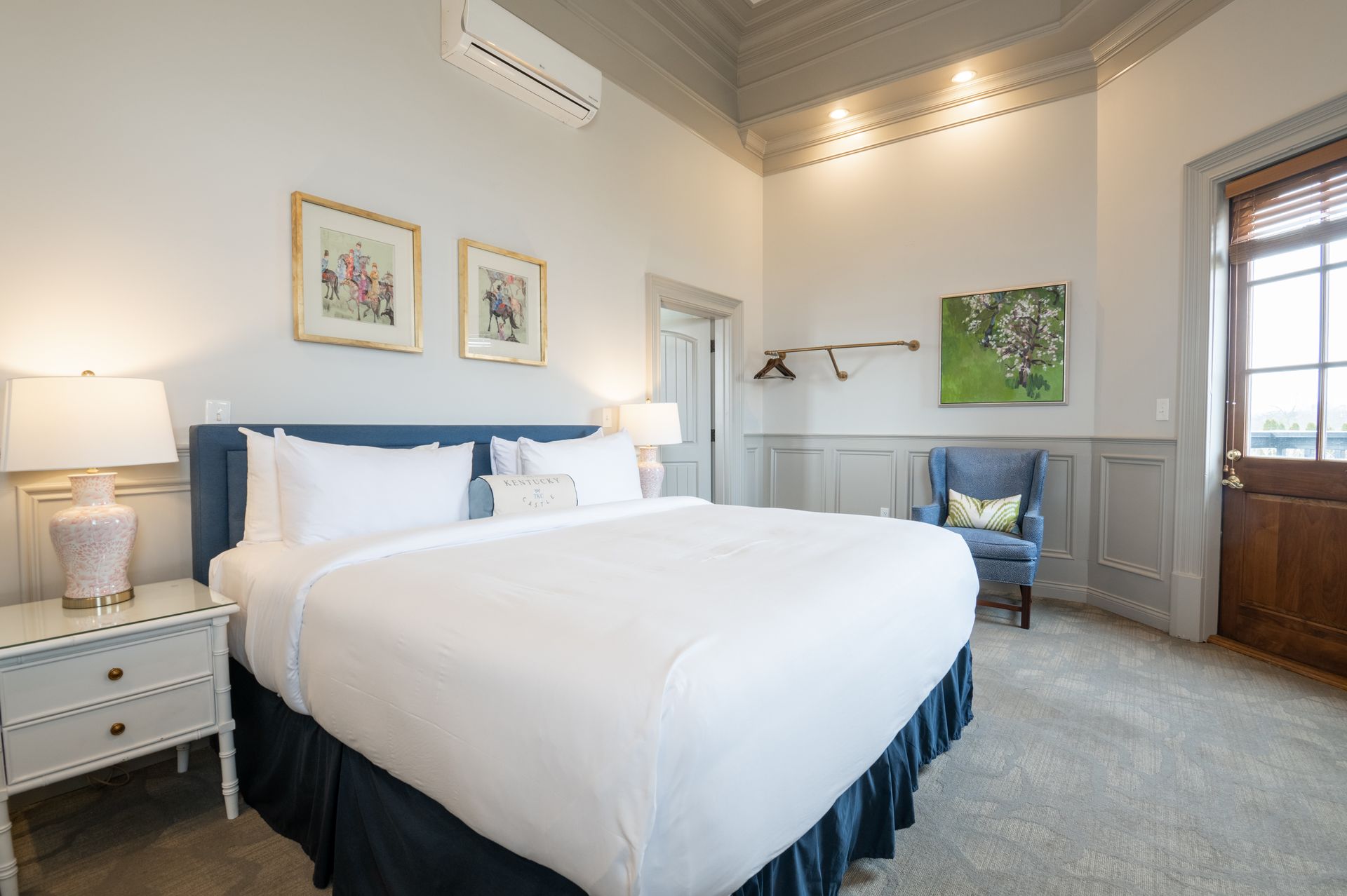 Bedroom with a large bed, blue accents, two framed floral prints, a chair, and a door.