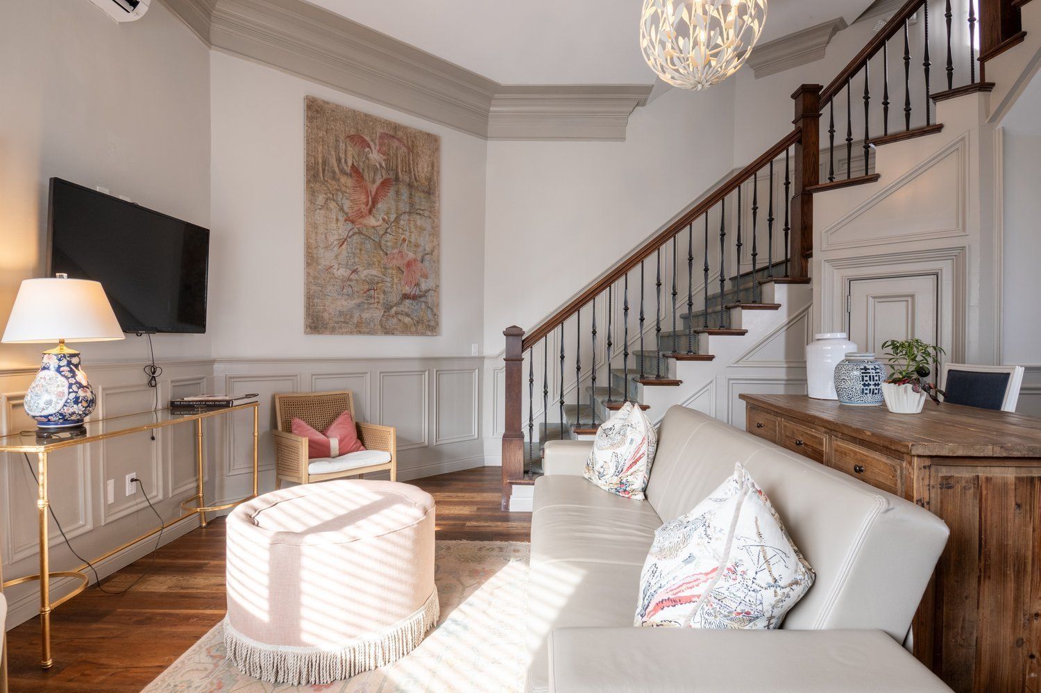 Living room with staircase, sofa, and artwork. Neutral tones with gold accents.