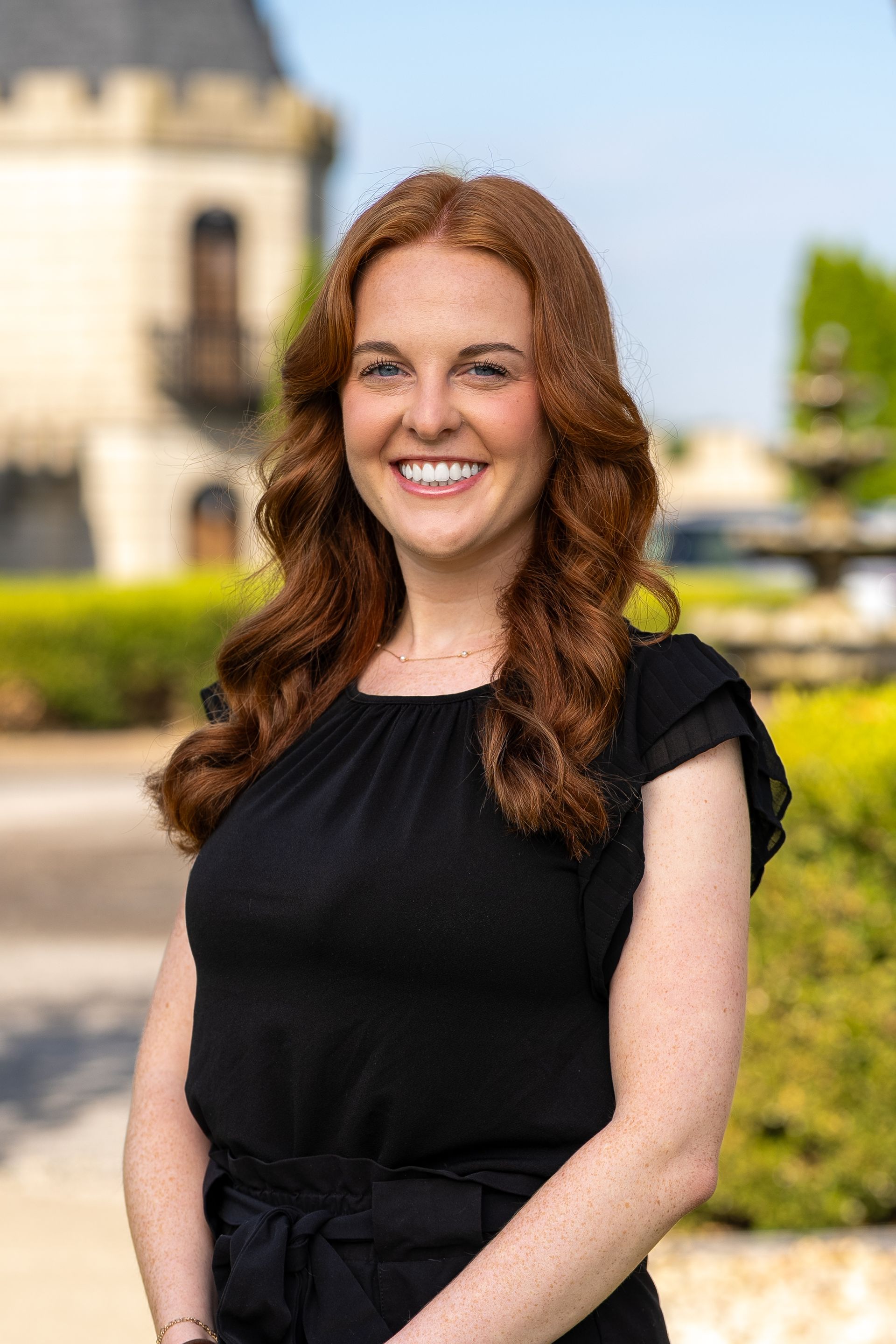 Woman with long brown curly hair in blue polka dot dress smiles, leaning on a marble counter.