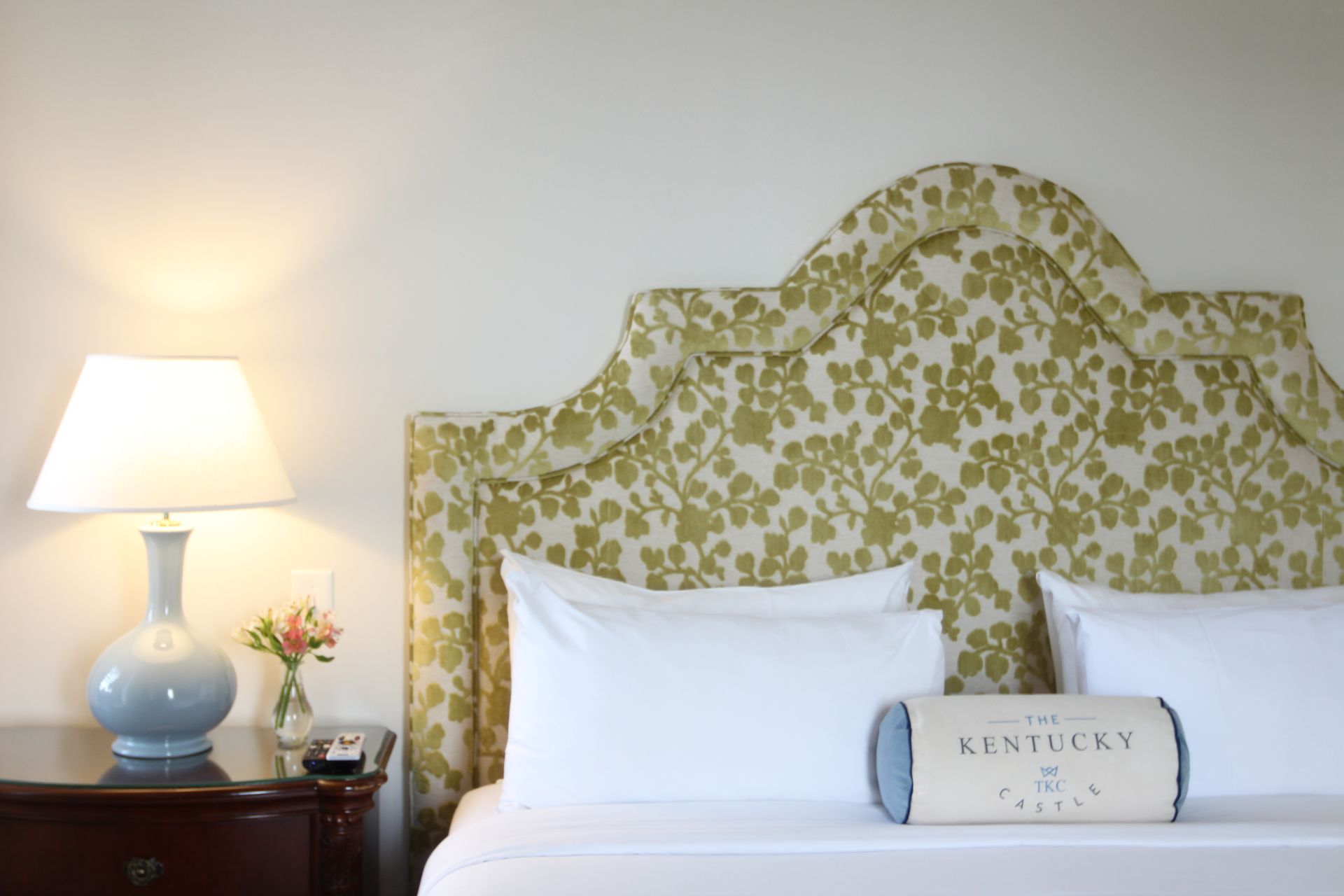 Bedroom with bed, floral headboard, nightstand with lamp, and decorative pillow.