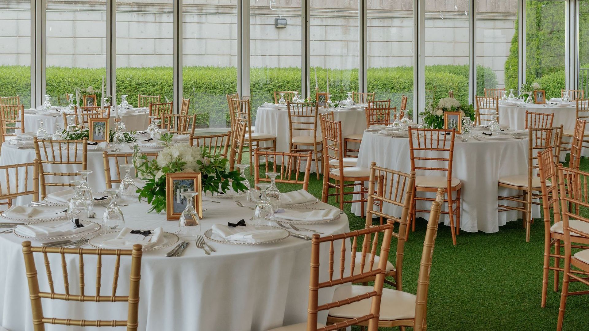 Wedding reception with round tables set with white linens, gold chairs, and greenery.