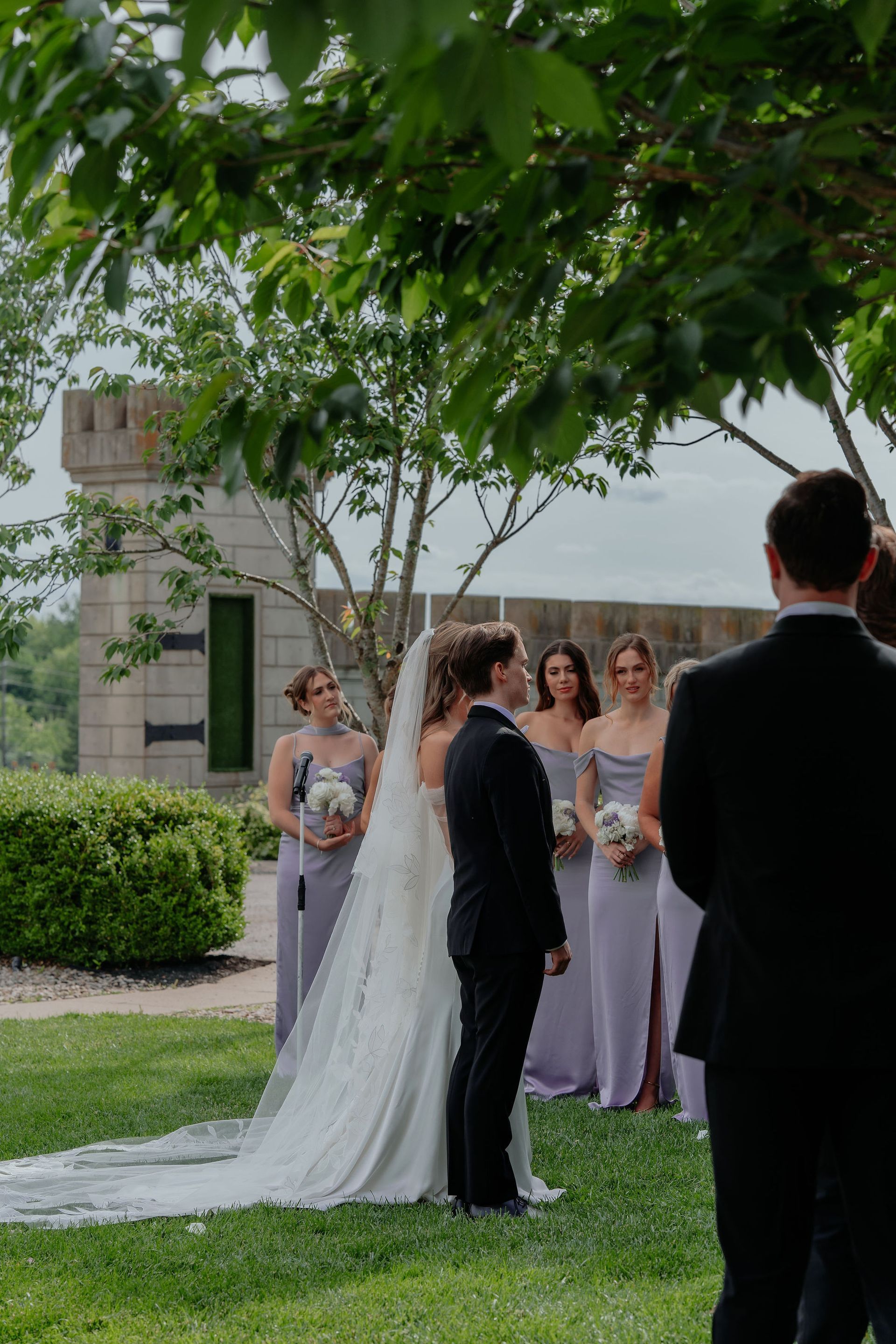 Wedding ceremony: Bride and groom at the altar, surrounded by bridesmaids in lavender dresses, and guests.