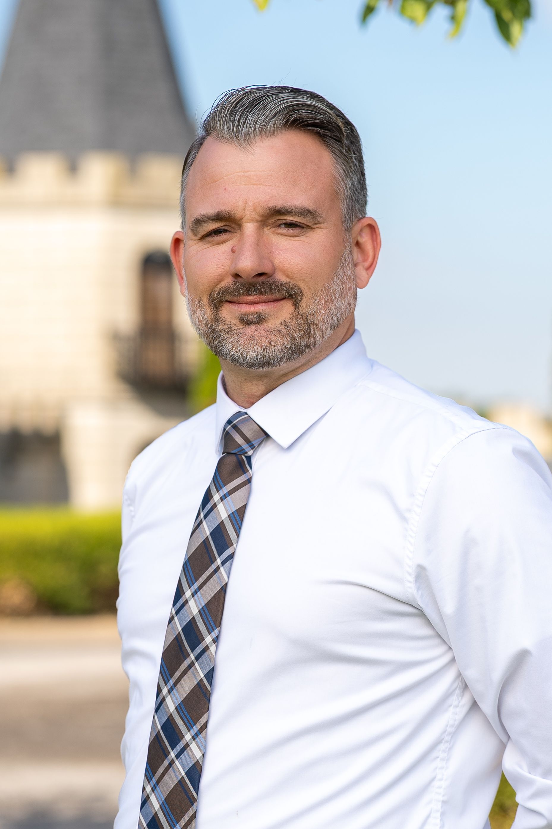 Man in gray suit and blue tie smiles in elegant, blurred interior.