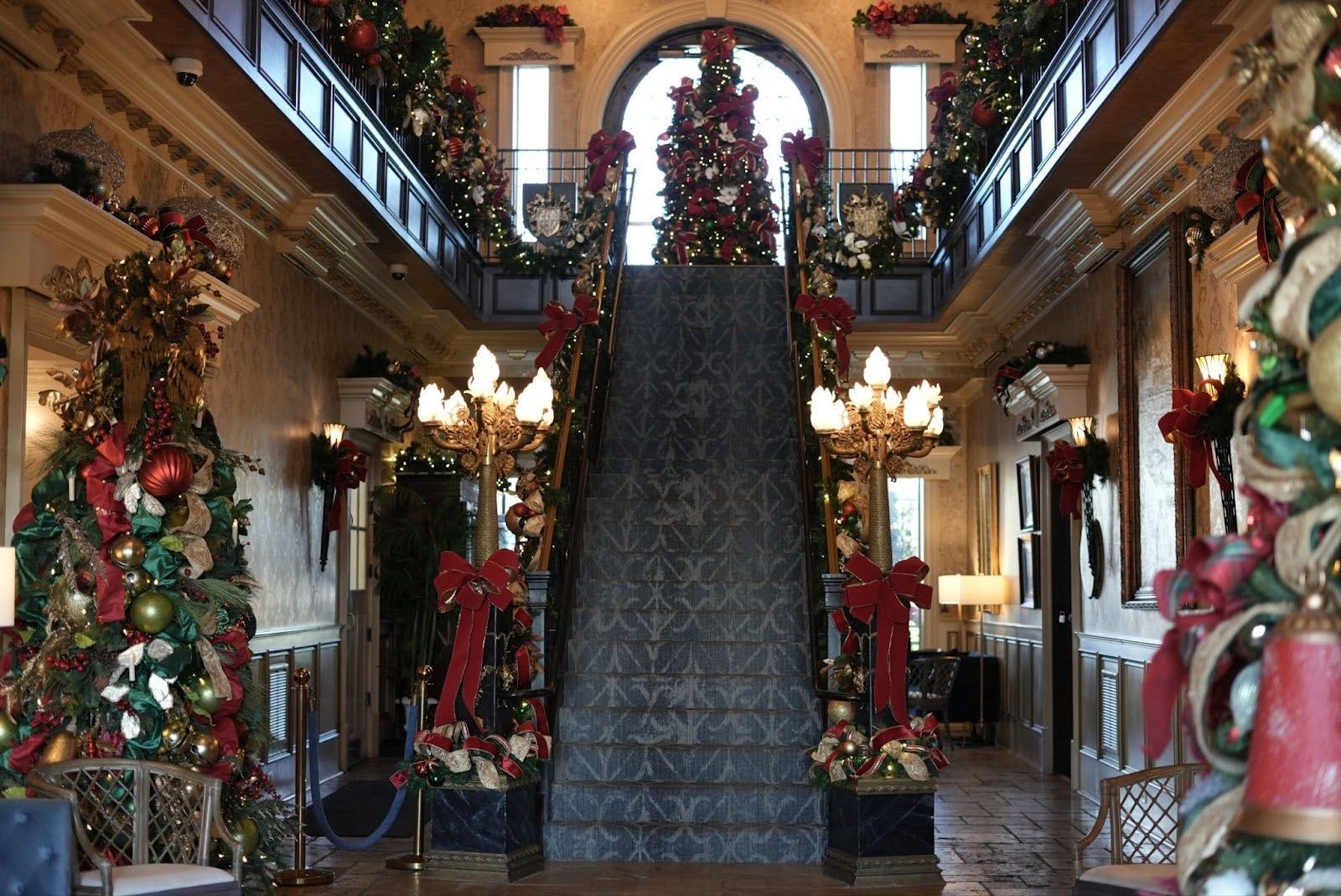 Grand hall decorated for Christmas with a staircase, trees, and red bows.