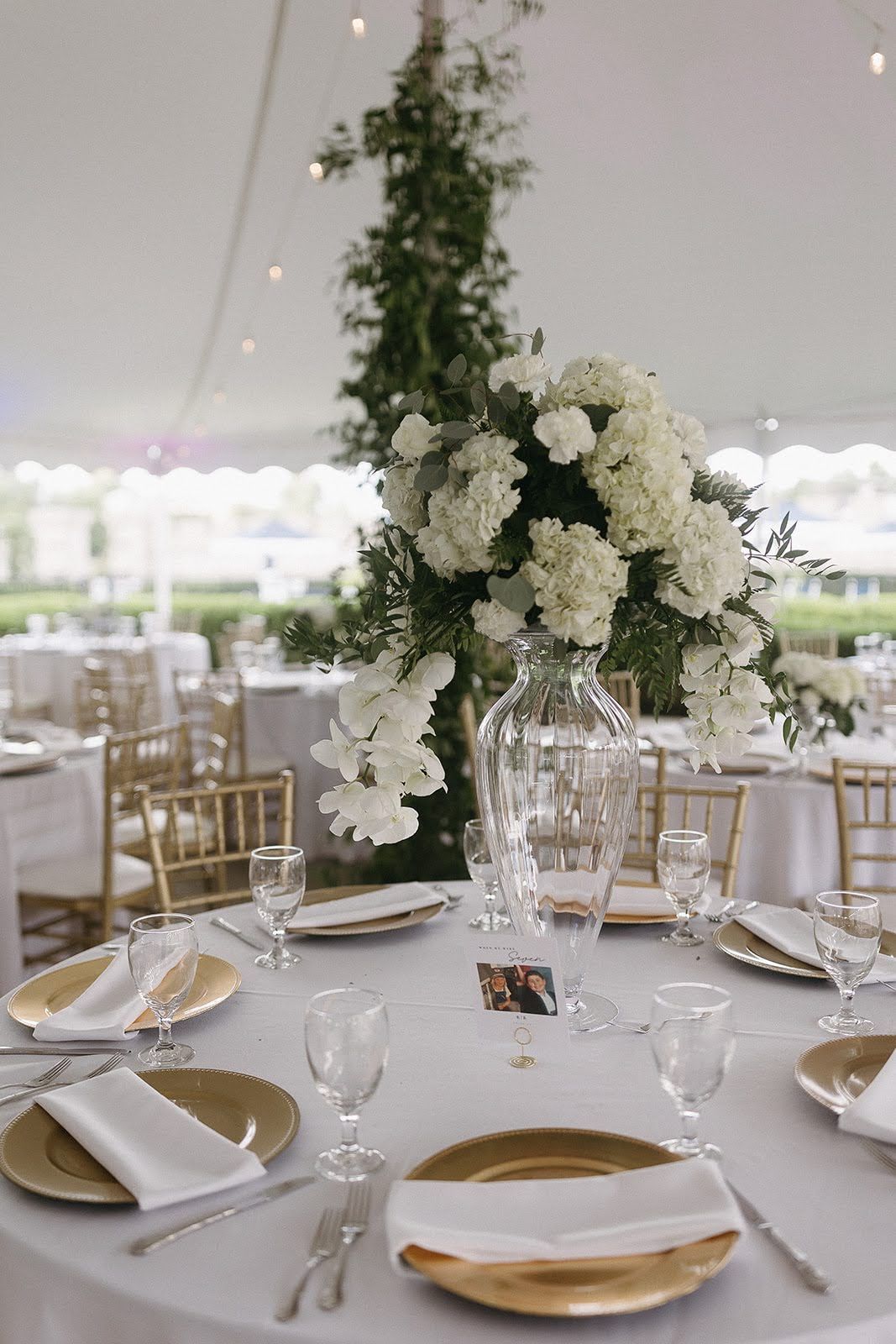 Wedding reception table with gold-rimmed plates, crystal vase floral centerpiece, and white linens.