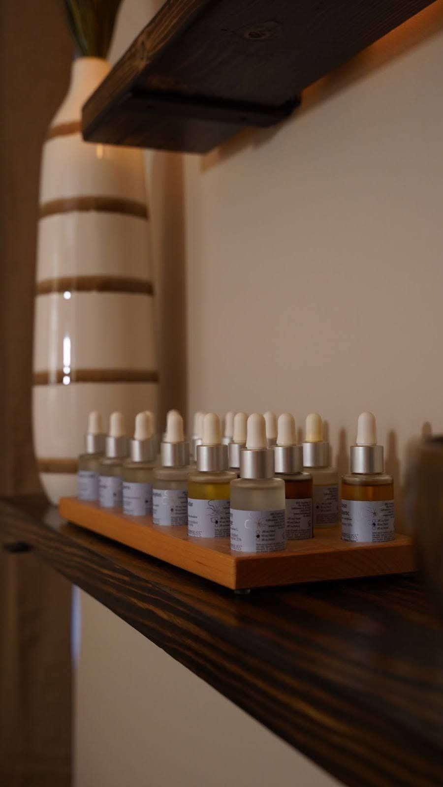 Bottles of oils on a wooden shelf, with a white and brown vase in the background.