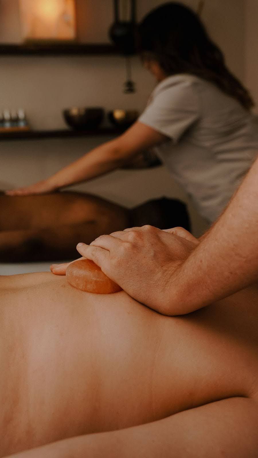 Two people receiving massages at a spa. Hands using a tool on back, with a masseuse in background.