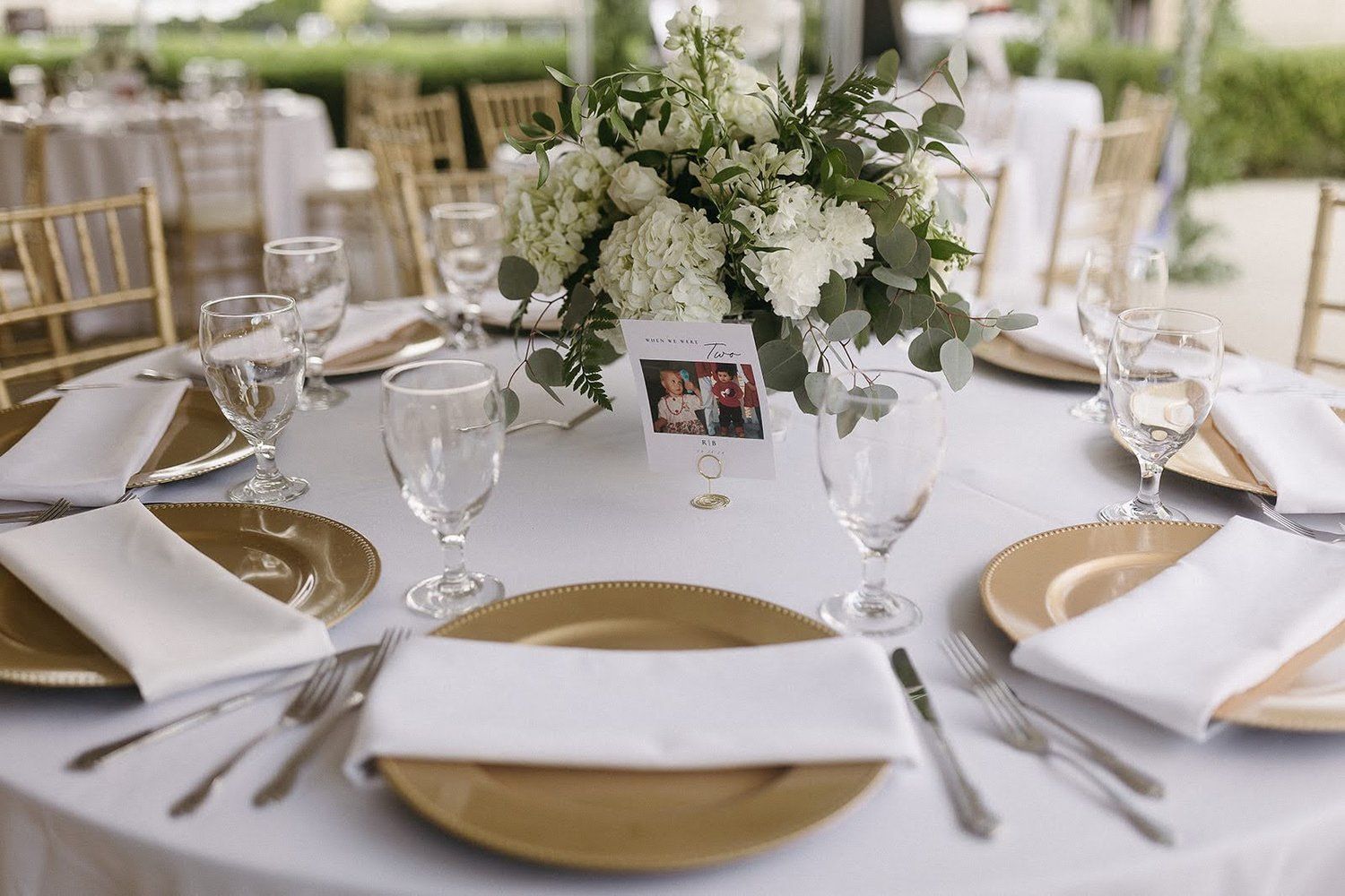 Elegant wedding reception table set with gold chargers, white napkins, and floral centerpiece.