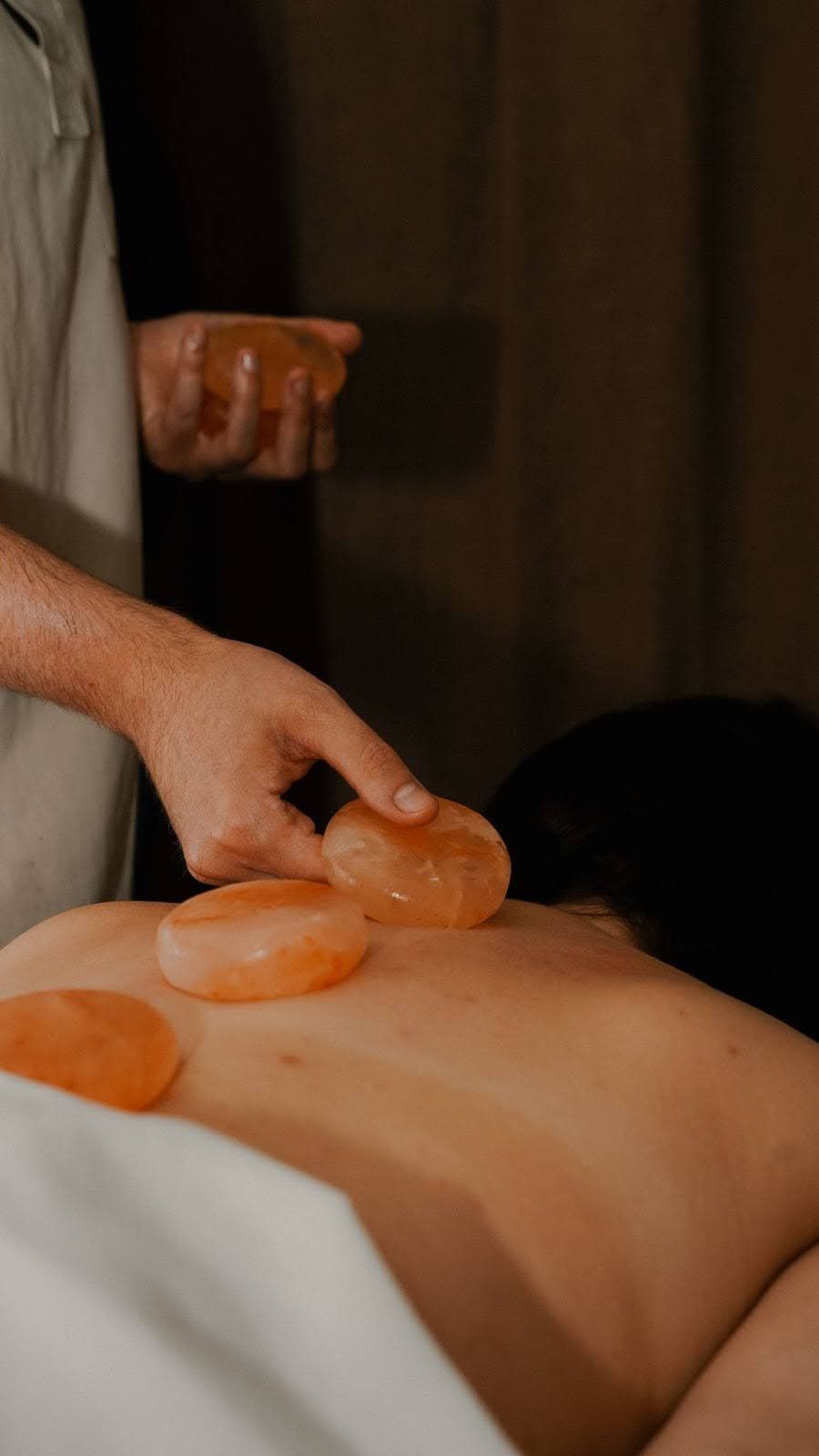 Person receiving a back massage with warm, orange salt stones in a spa setting.