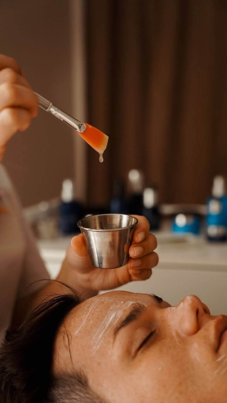 Facial treatment: A person's face with a brush applying liquid from a small metal bowl.