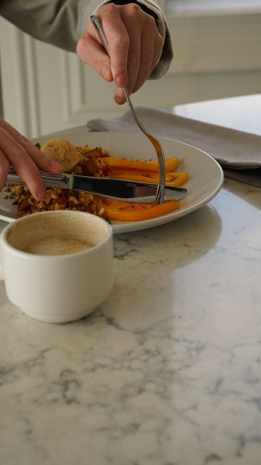 Person eating a meal of orange slices and a cup of coffee, plate on a marble table.