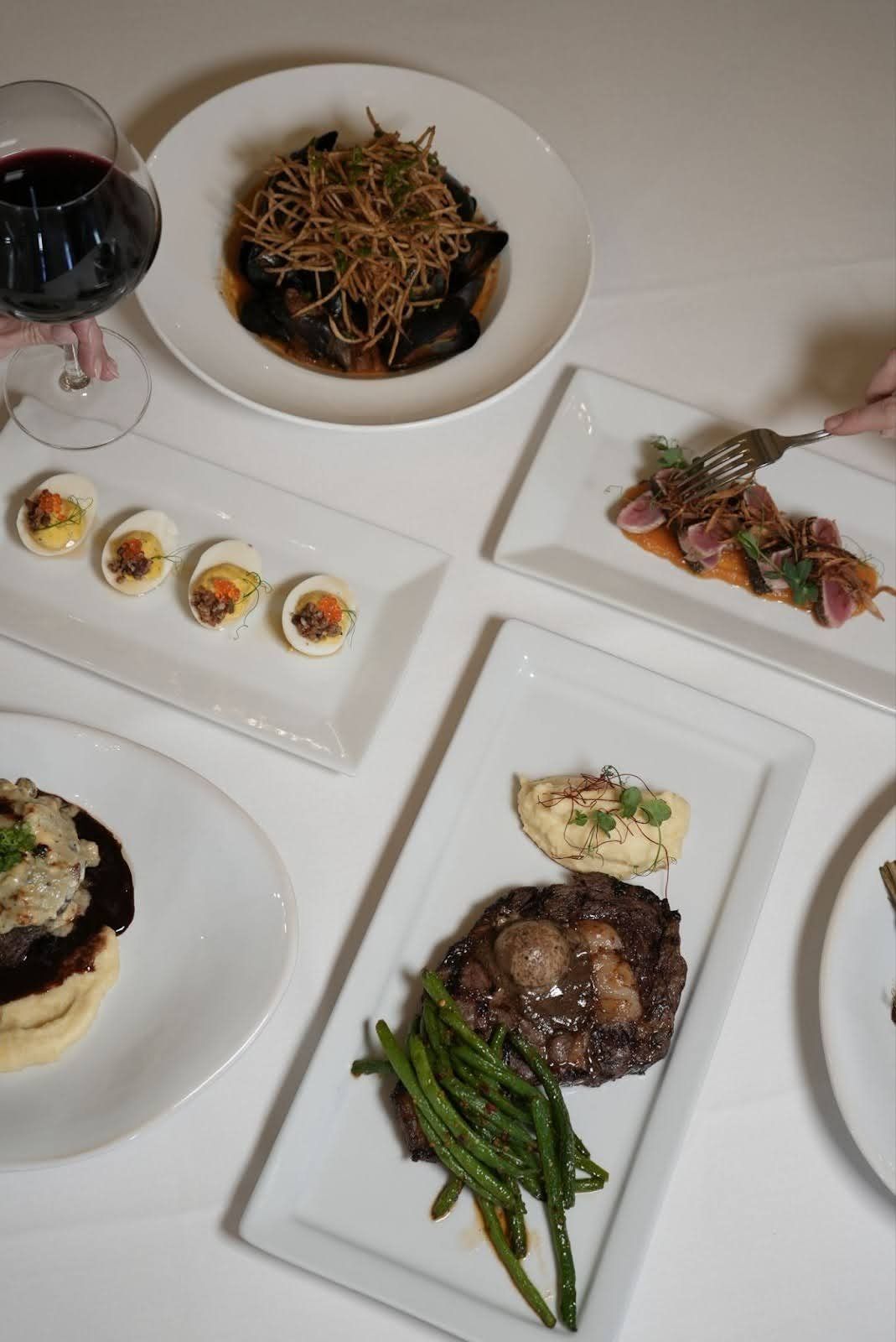 Platter of gourmet dishes including steak, tuna, deviled eggs, and a glass of red wine.