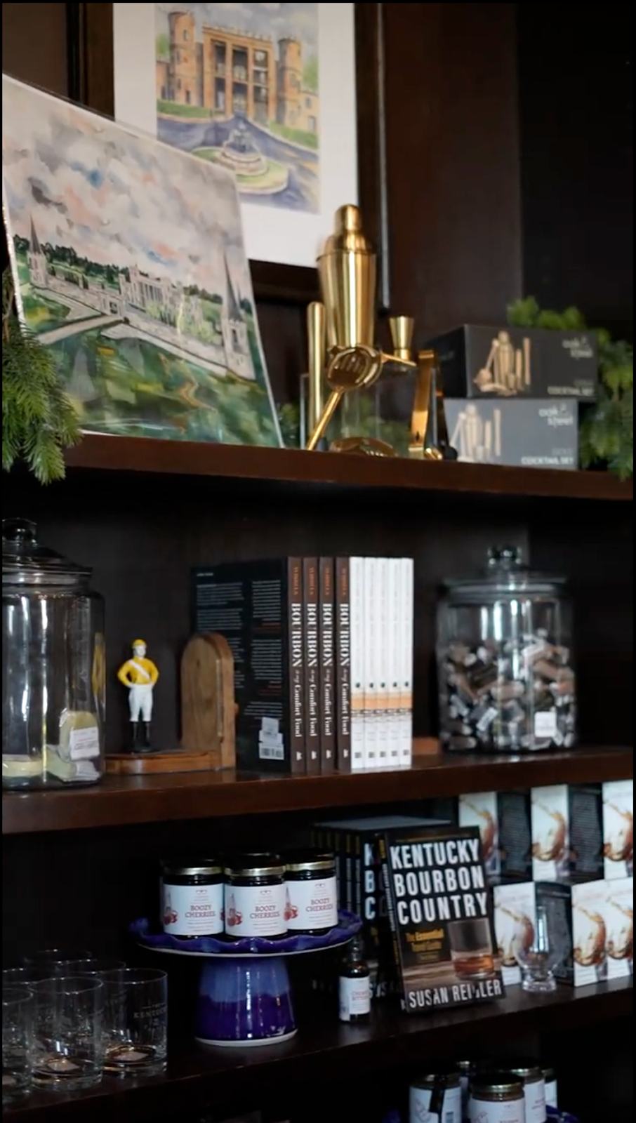 Wooden shelves holding jars, books, artwork, and barware in a dimly lit interior.