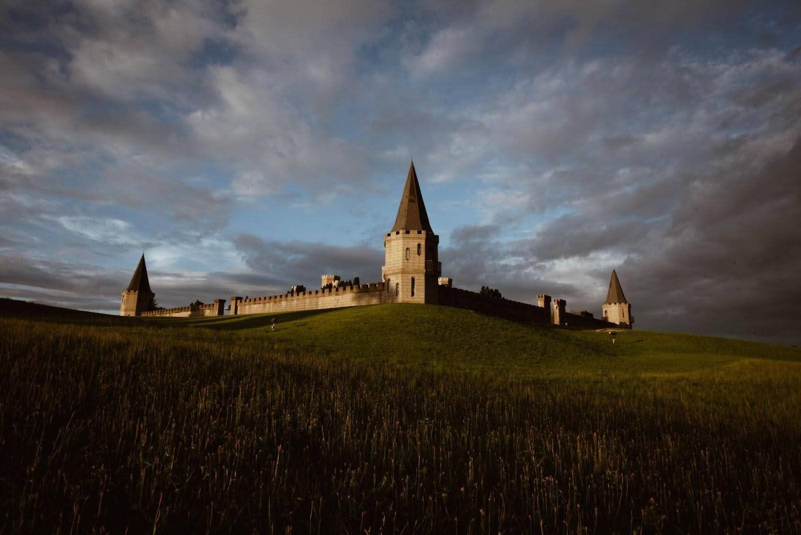 Castle on a grassy hill under a cloudy sky. Towers with spires, stone walls.