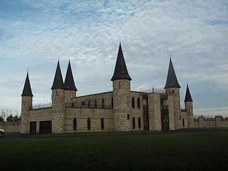 Stone castle with black spires on a grassy field under a cloudy sky.