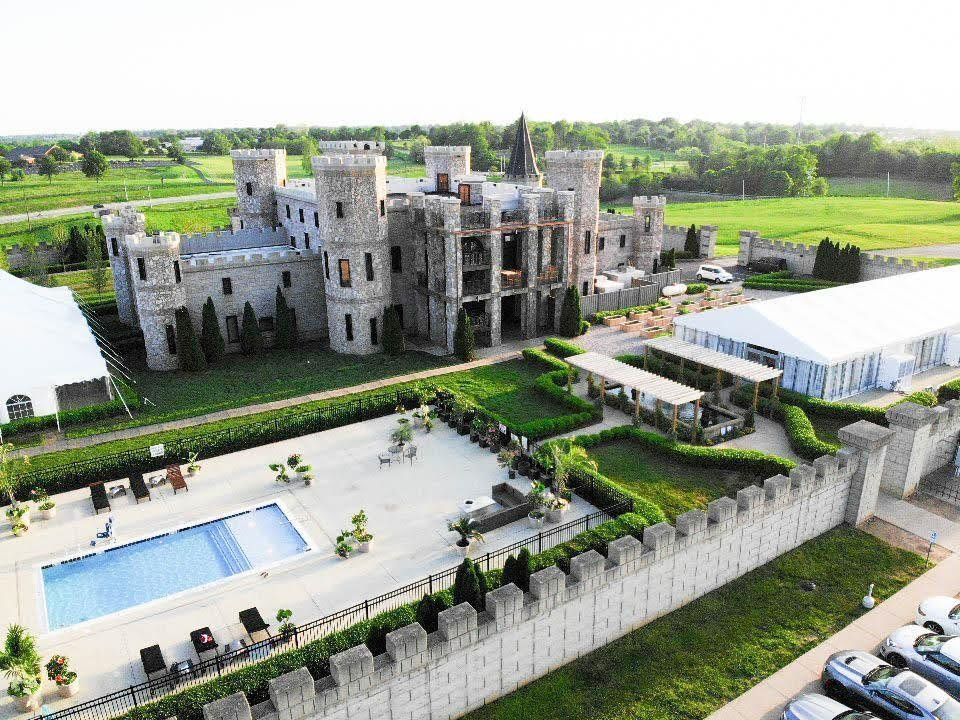 Stone castle with a pool, white tents, and a green lawn.