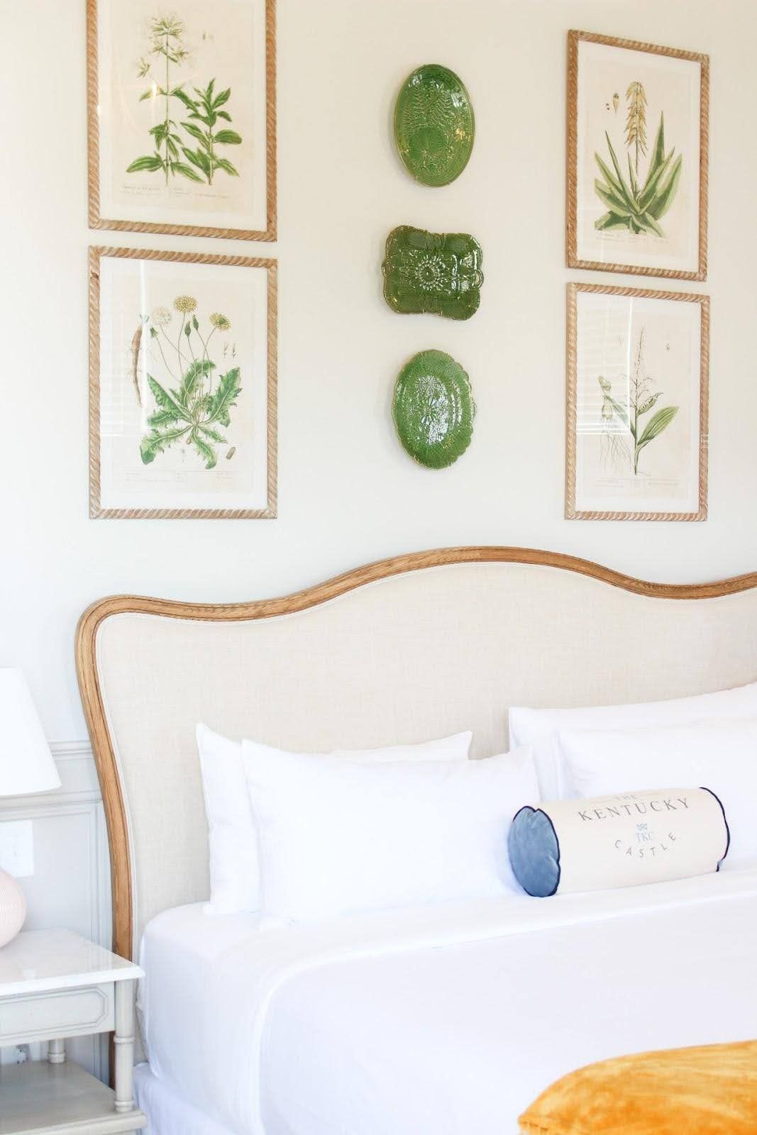 Bedroom with a light-colored headboard, white bedding, floral art, and green wall decor.